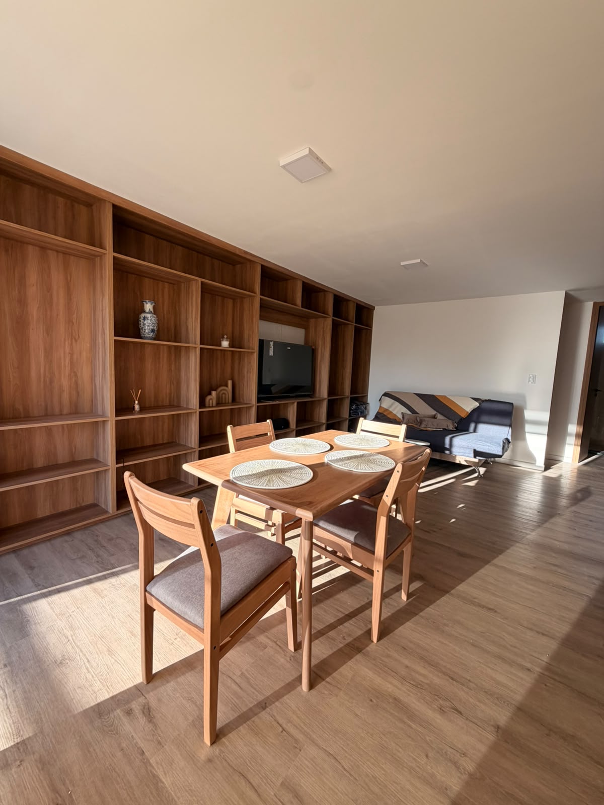 Comedor de Alma Urbana con mesa de madera, cuatro sillas y living al fondo